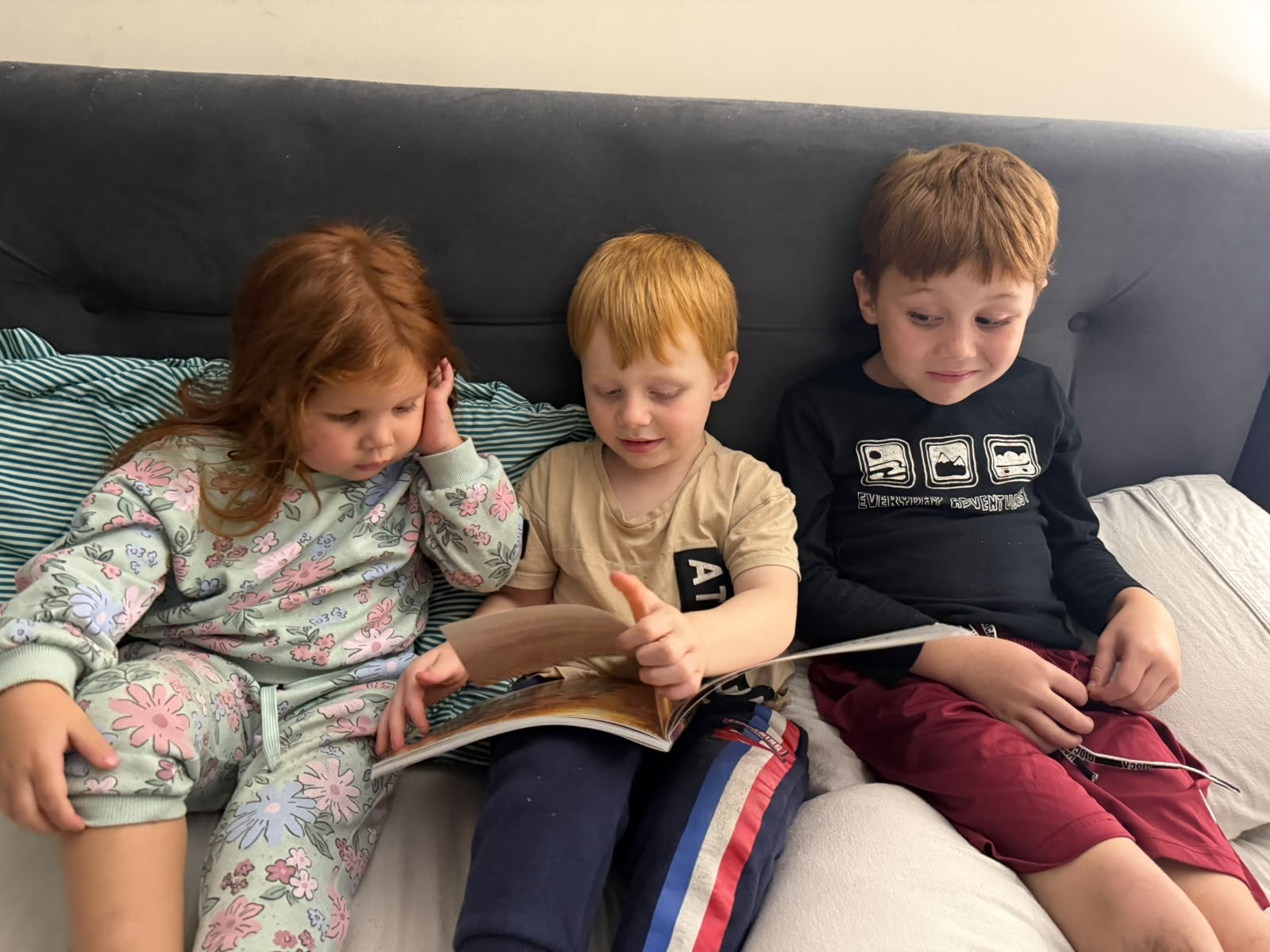 Three siblings sitting together and sharing a Monarch Tales storybook